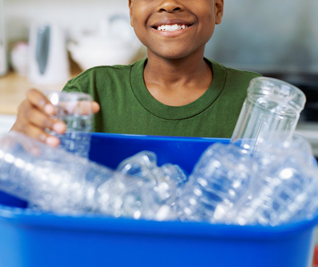 child placing plastic bottle in recycle bin